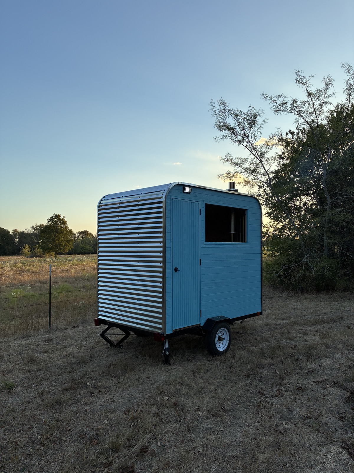 Rear three-quarter view of the sauna trailer showing corrugated steel siding and the entry door