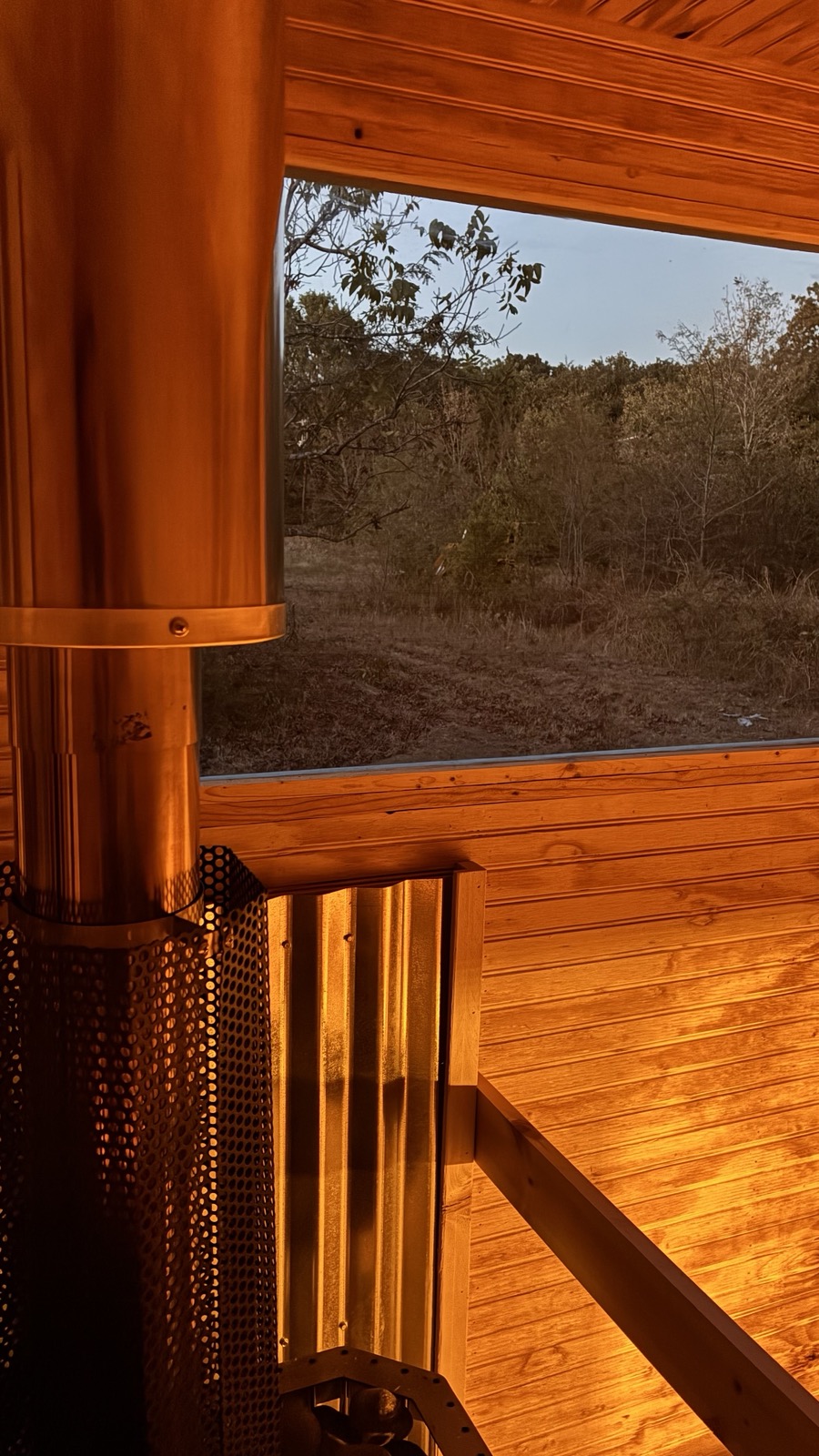 View from inside the sauna: pine walls, chimney, and a window onto open woods