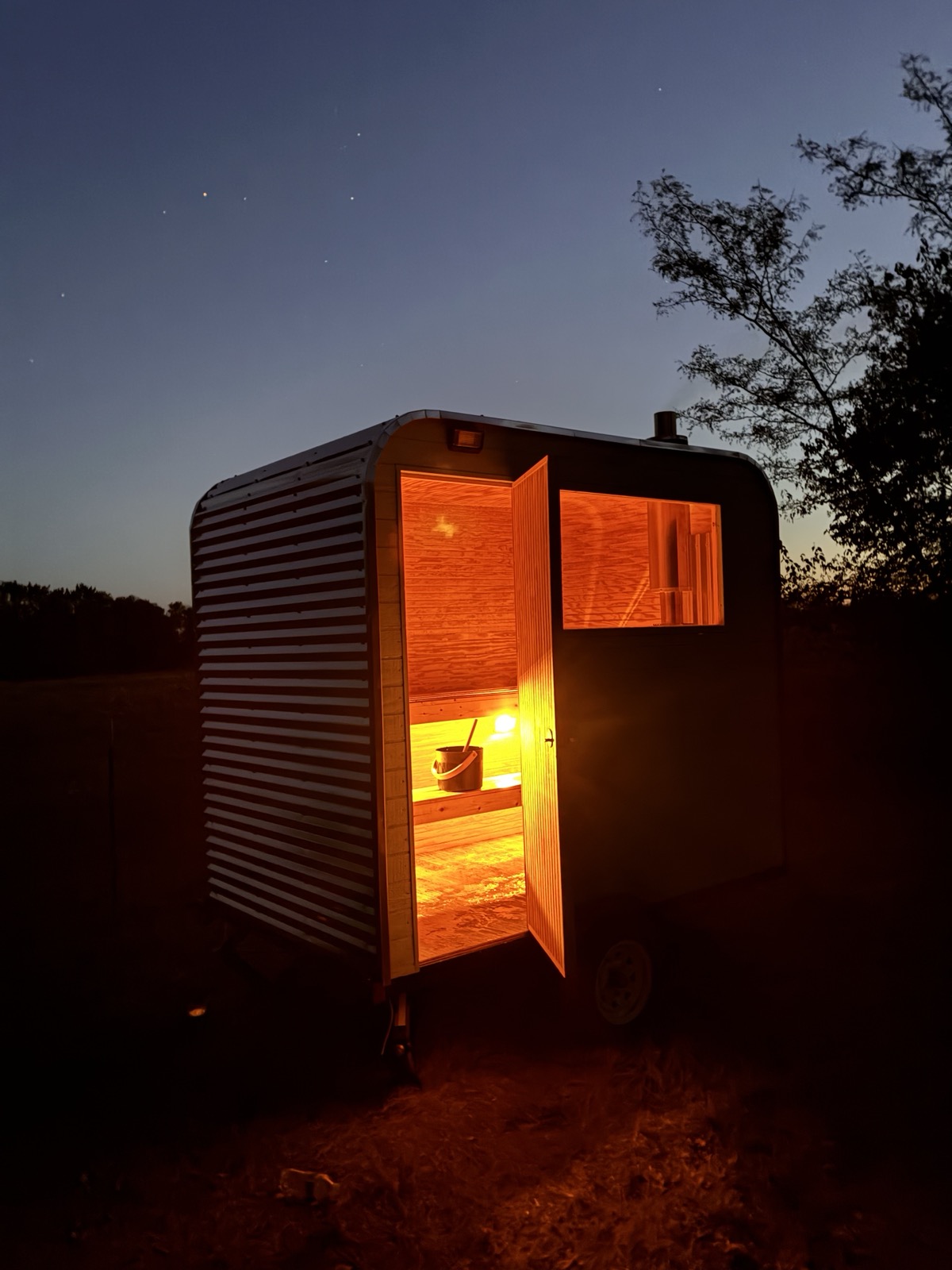 Sweatystoves sauna trailer glowing at dusk with the door open under a starry sky
